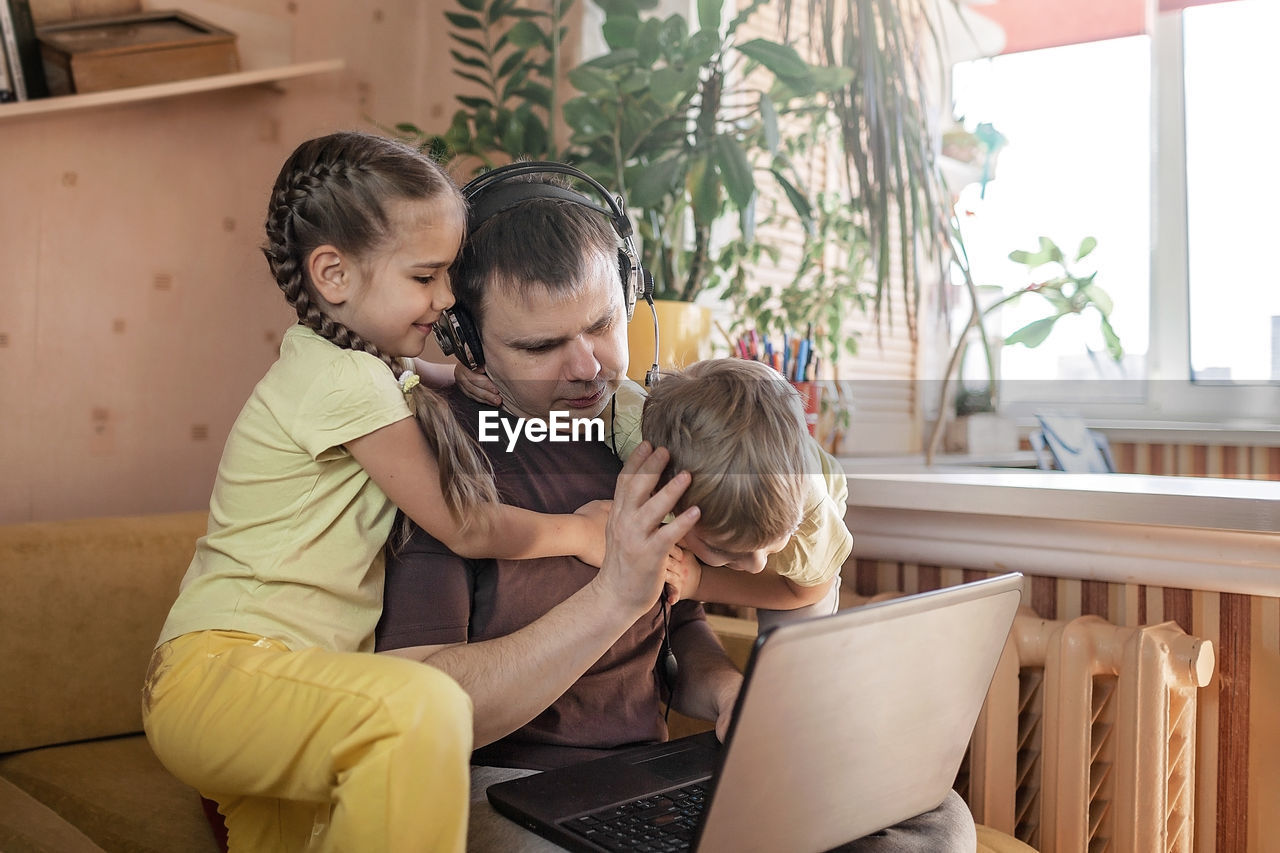 REAR VIEW OF MAN USING PHONE WHILE SITTING ON LAPTOP