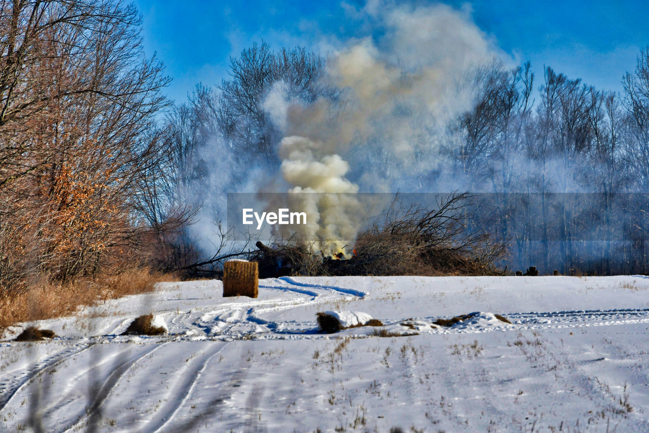 Smoke emitting from land against sky during winter