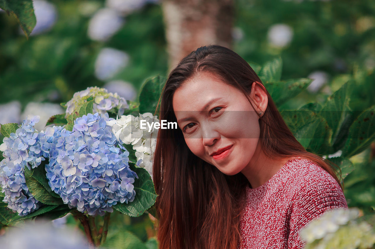 PORTRAIT OF SMILING YOUNG WOMAN WITH PINK FLOWER