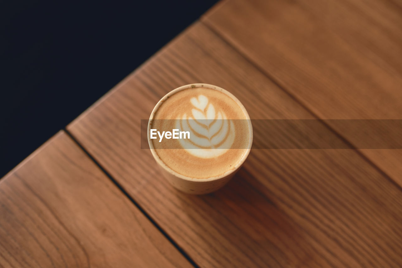 Cup of cappuccino with latte art on the wooden table. beautiful foam and ceramic cup