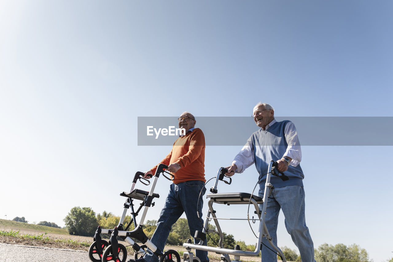 Two old friends walking on a country road, using wheeled walkers