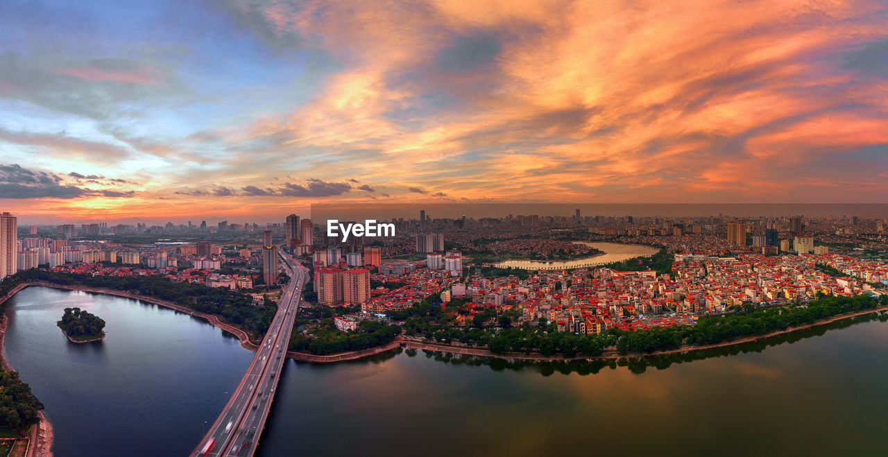 Aerial view of bridge over river and buildings against sky during sunset