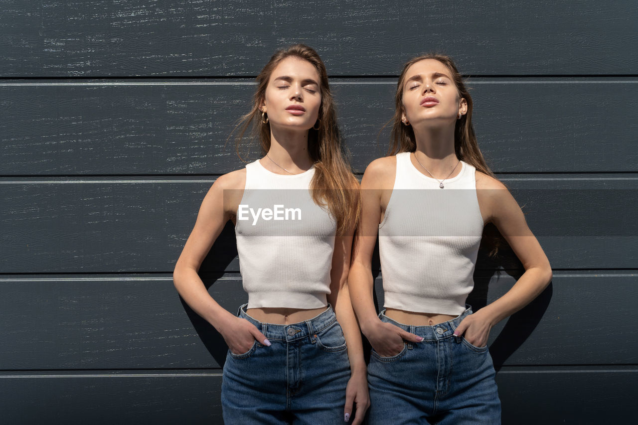 Women with closed eyes standing against wall