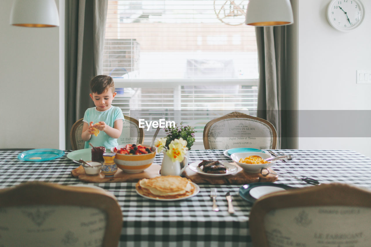 Boy having breakfast while sitting on table at home