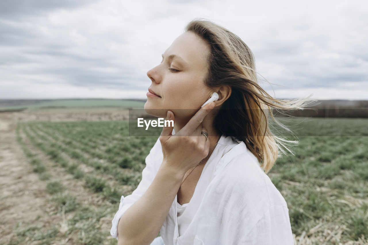 Woman with eyes closed adjusting in-ear headphones at agricultural field