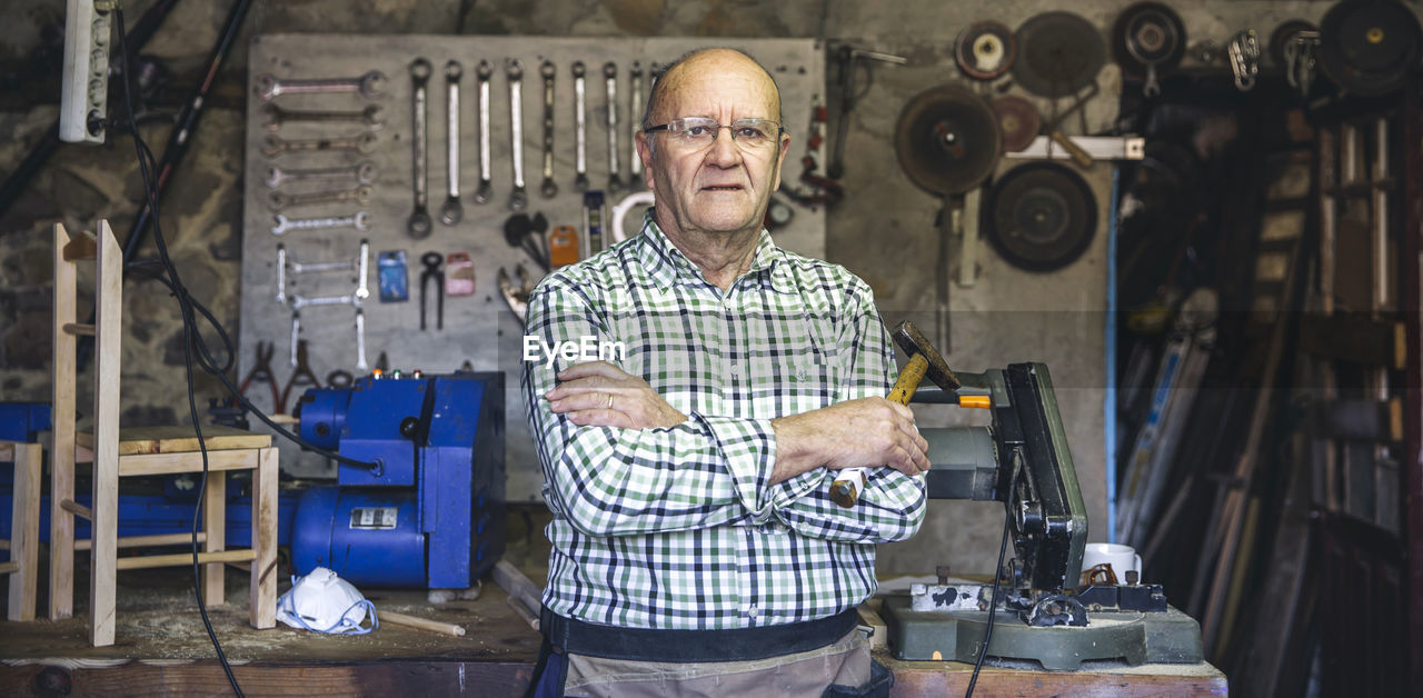 Portrait of smiling senior man with arms crossed standing in workshop