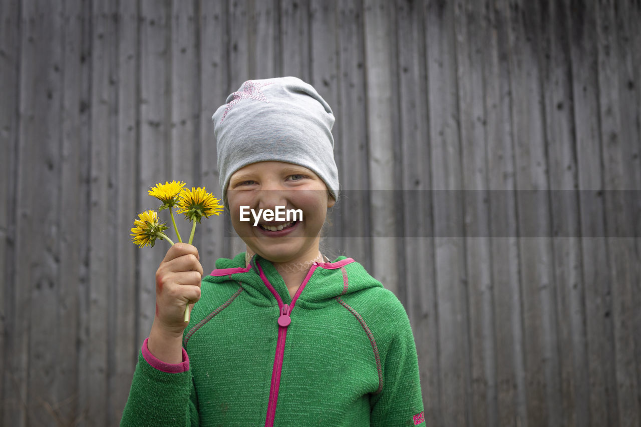 Portrait of smiling boy holding flower standing outdoors