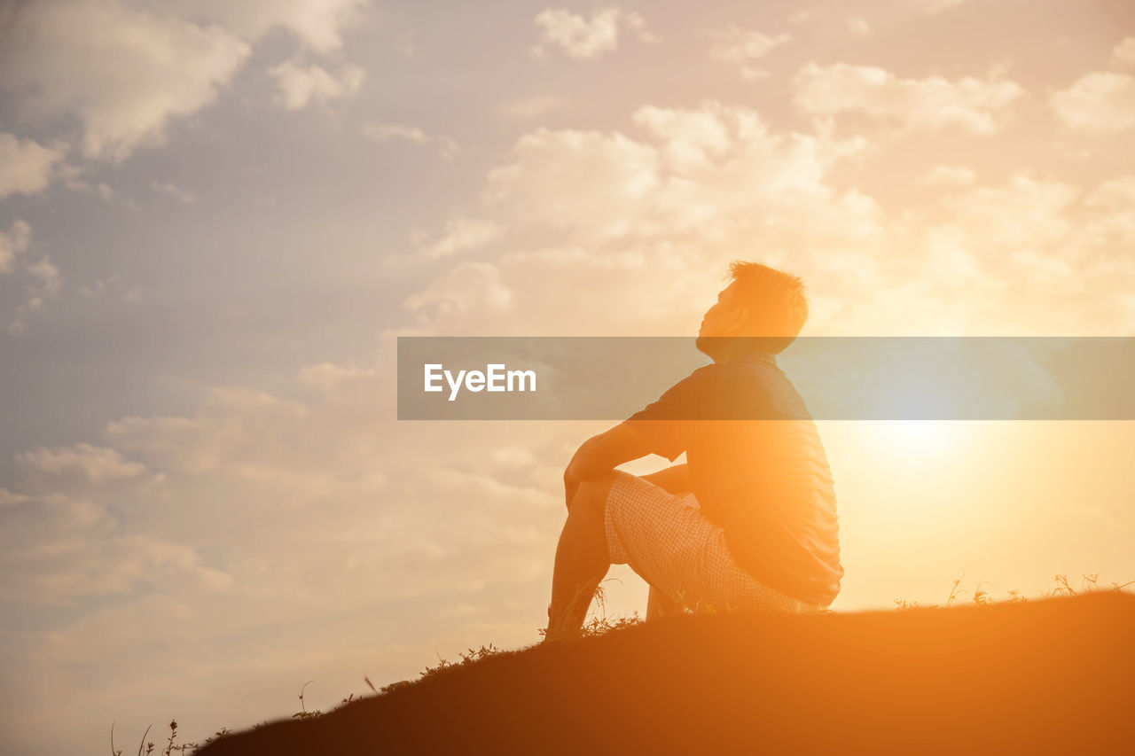 Side view of silhouette man sitting against sky during sunset