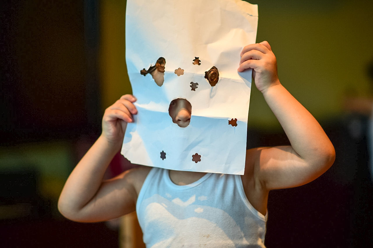 Close-up of child looking through holes in paper