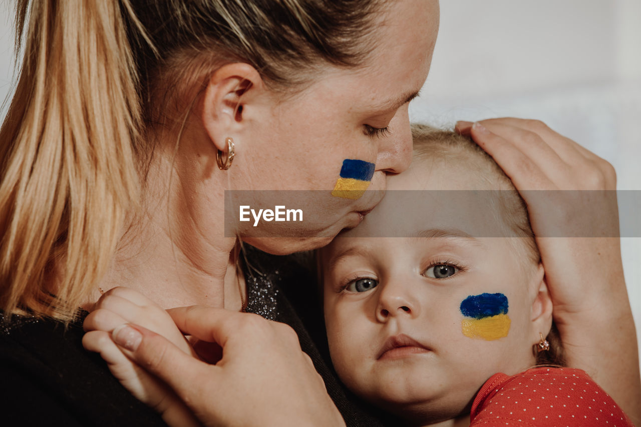 Mother kissing daughter with ukrainian flag paint on face