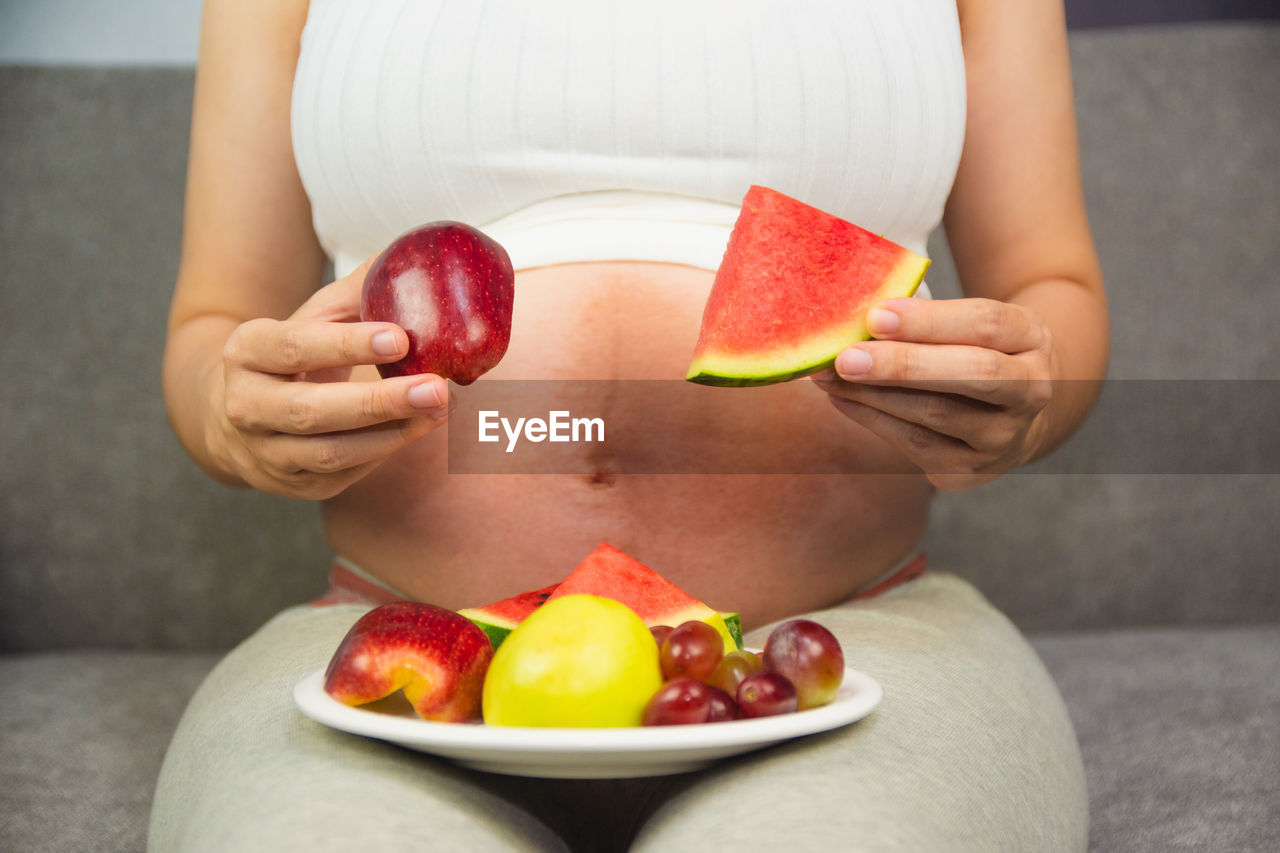 MIDSECTION OF WOMAN HOLDING RED FRUIT