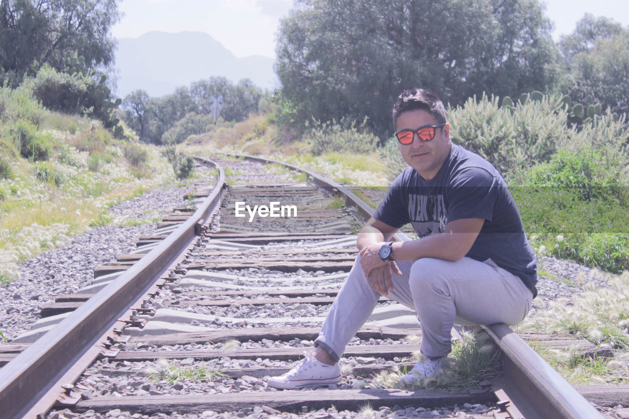 YOUNG MAN SITTING ON RAILROAD TRACK