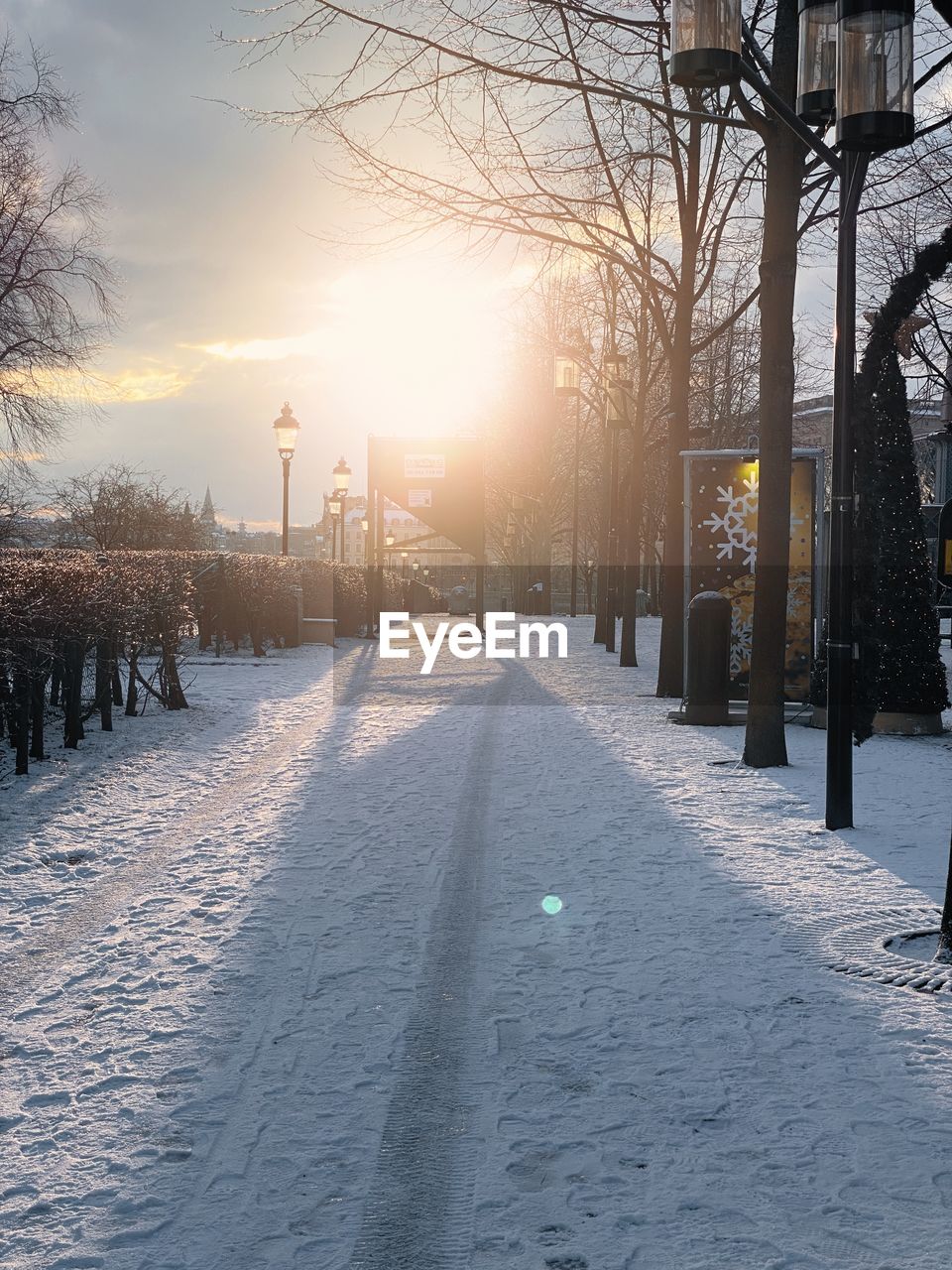 Snow covered street against sky during sunset