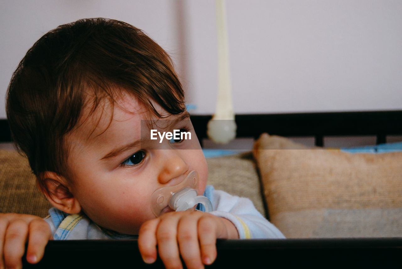 Close-up of baby boy with pacifier in mouth looking away at home