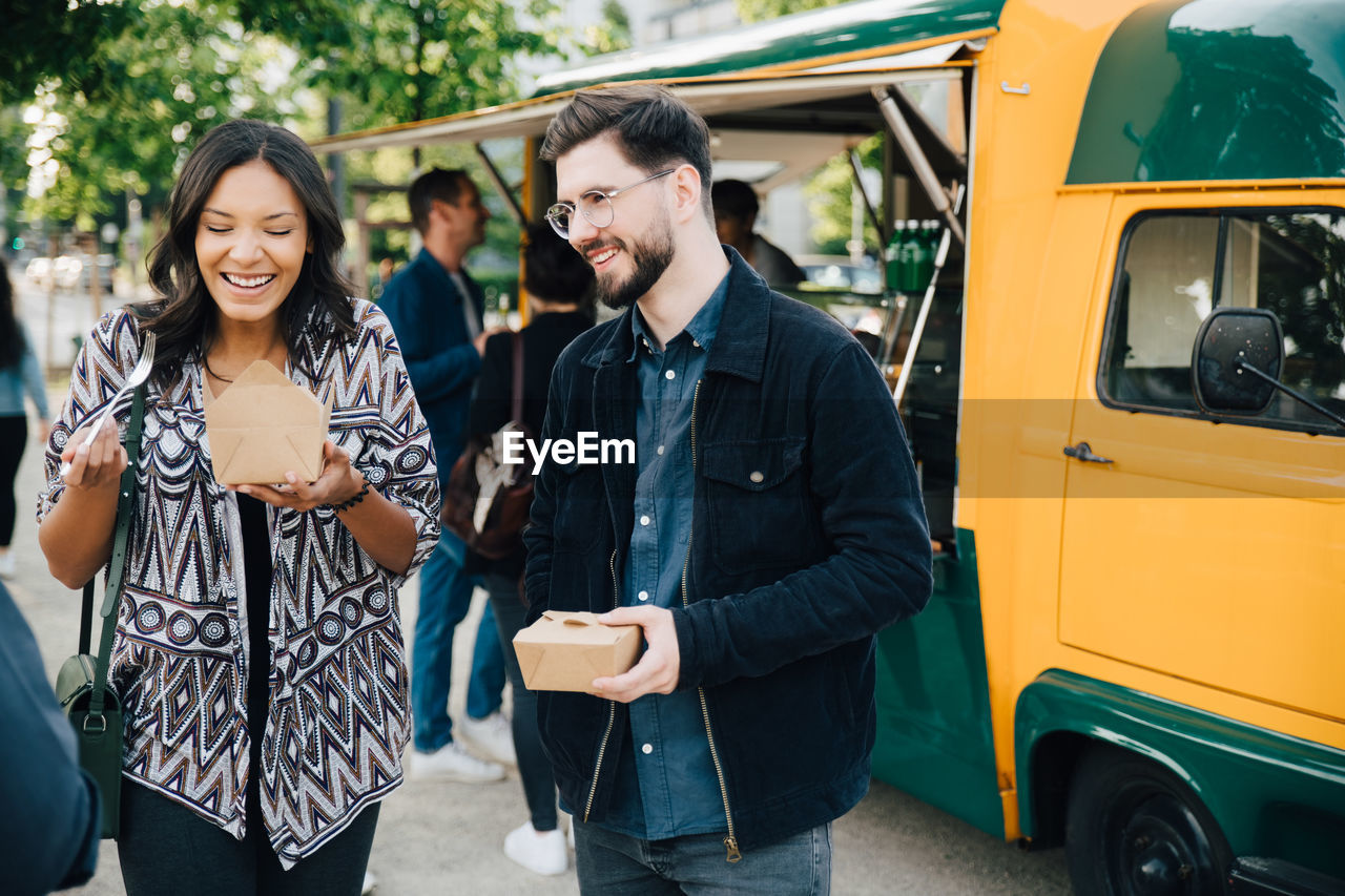 Female laughing while standing by male friend with box against food truck