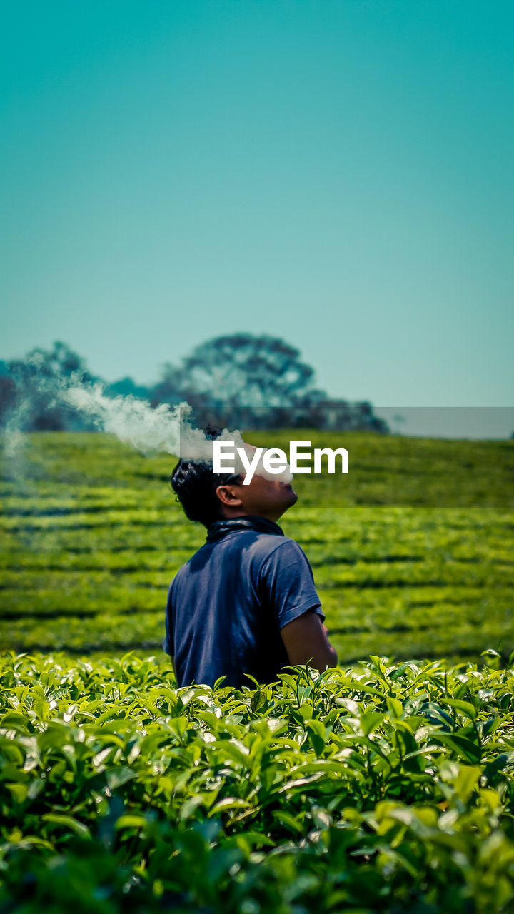 Man emitting smoke while standing amidst plants