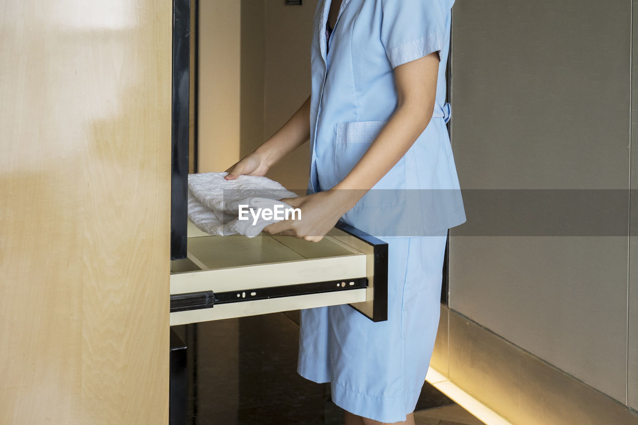 Midsection of woman holding towel above cabinet drawer