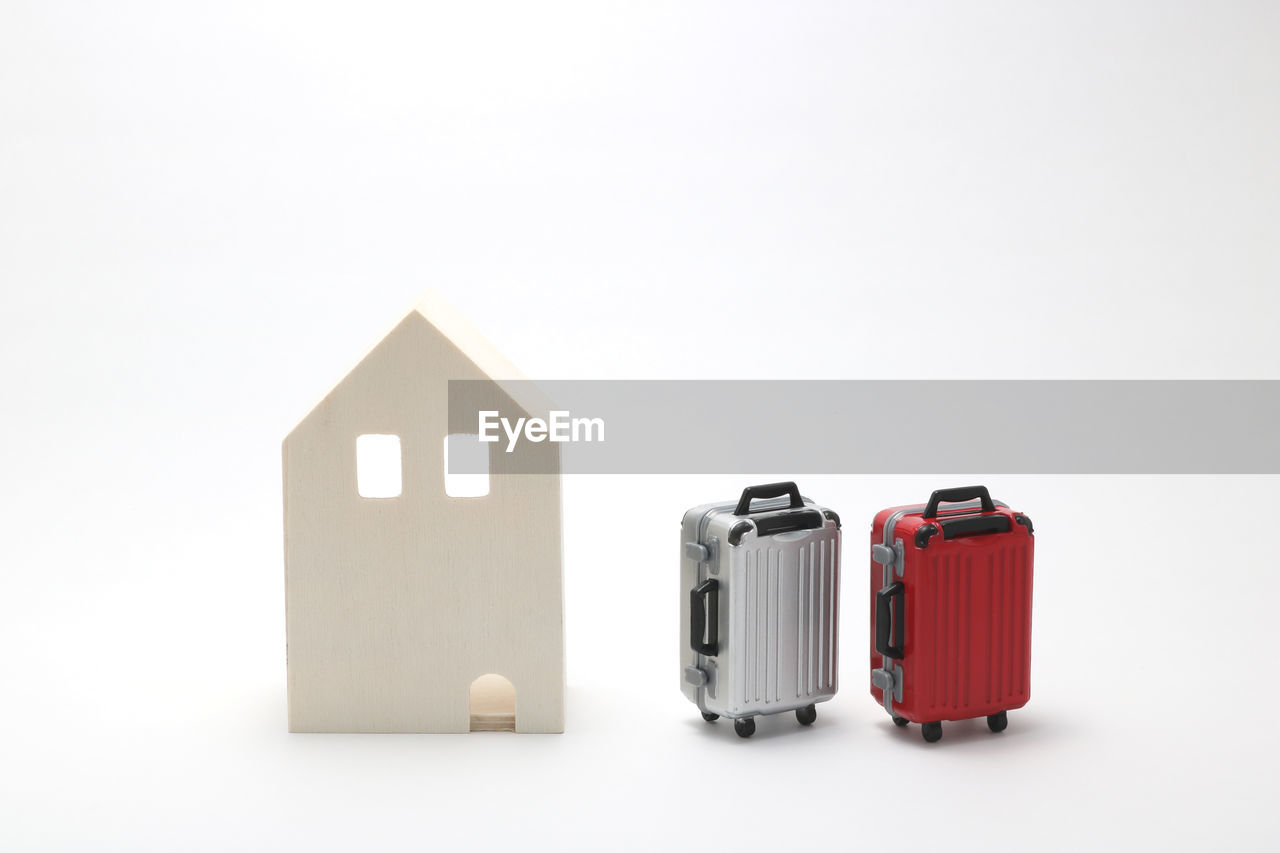 Close-up of model home by small suitcases against white background