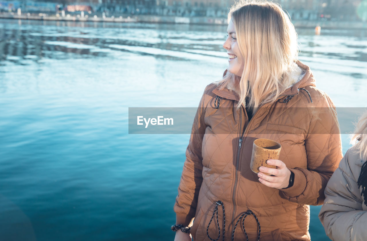 Smiling woman at waterside holding mug after cold swim in denmark