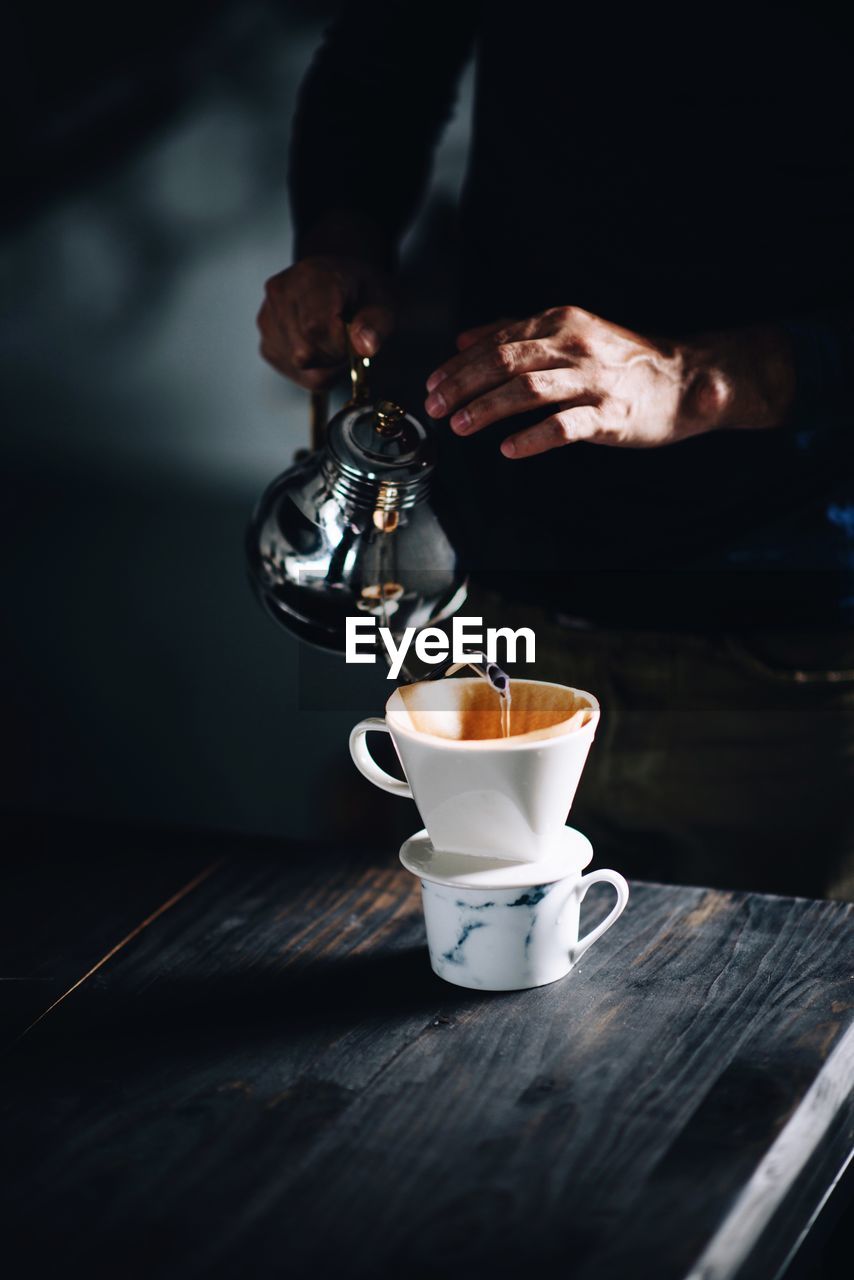 Close-up of hand pouring coffee in cup on table