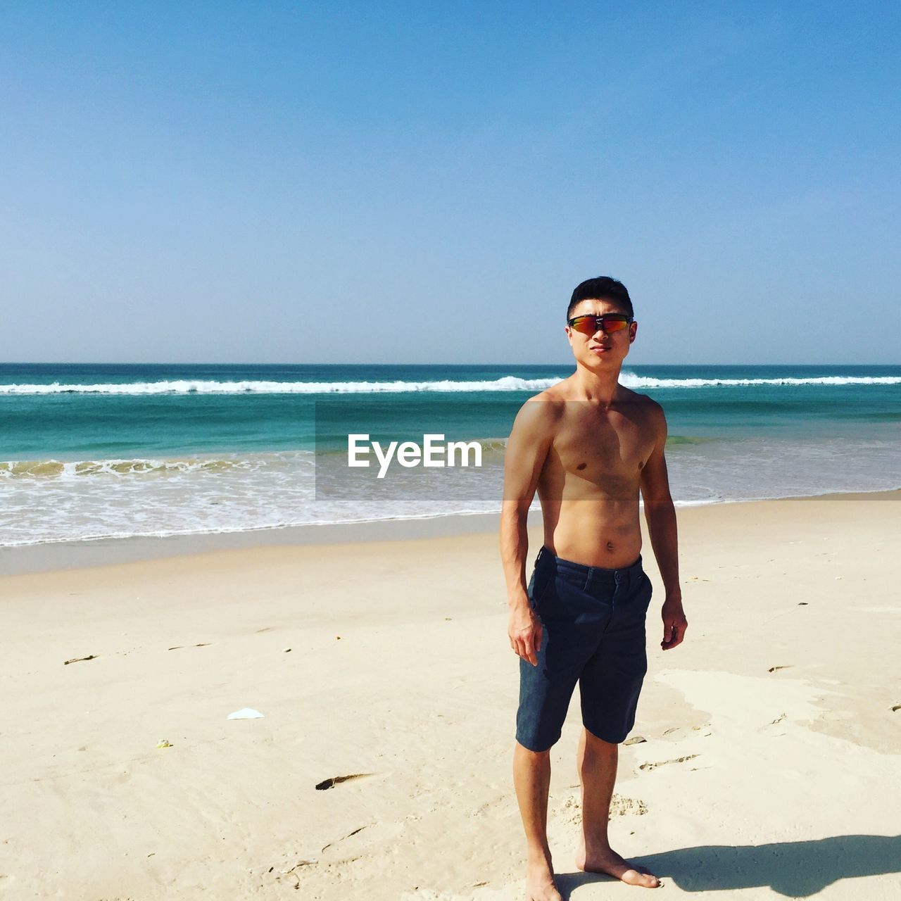 Portrait of shirtless man standing on shore at beach against sky