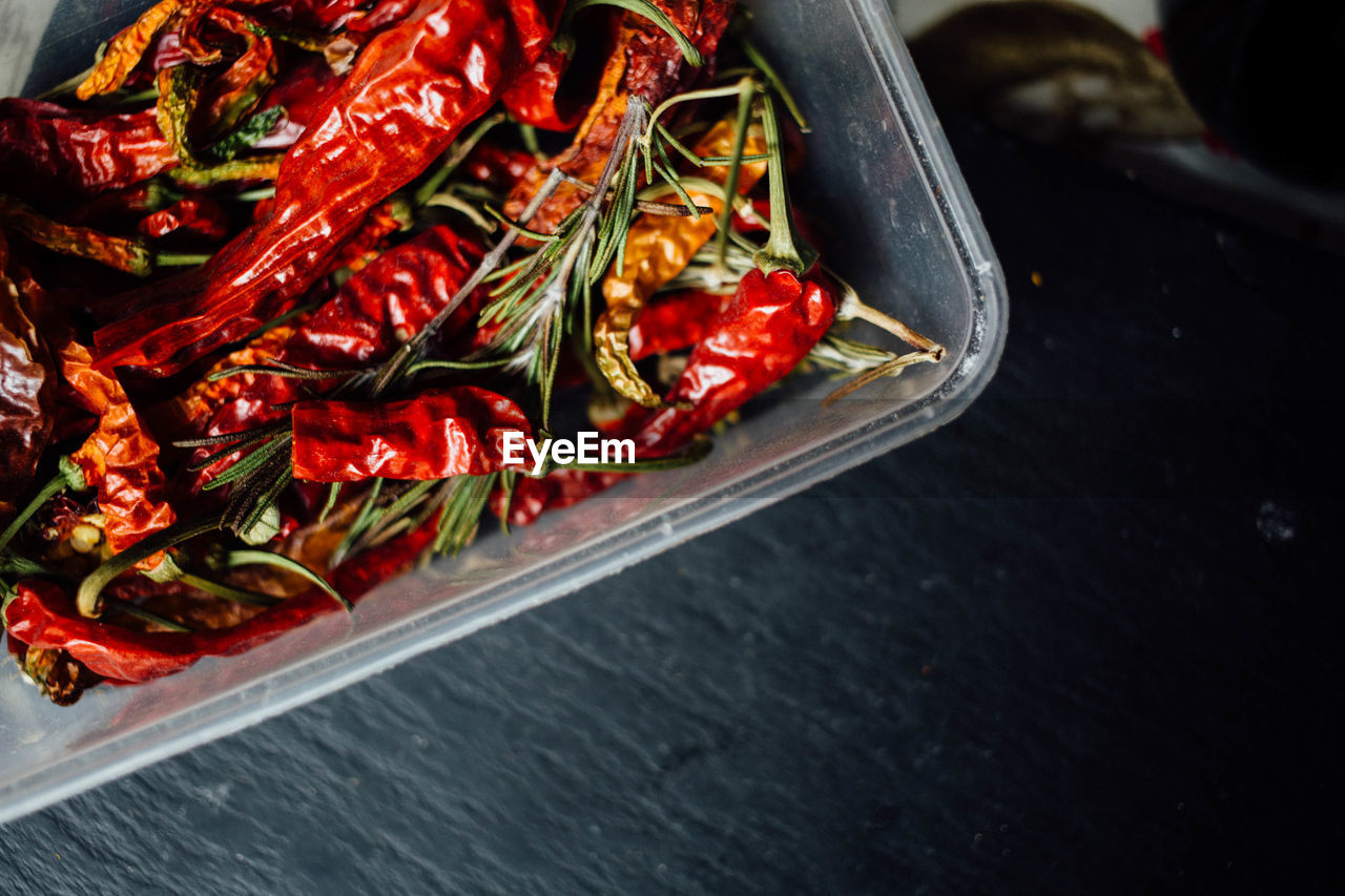 Directly above shot of red chili peppers and rosemary leaves in container on table