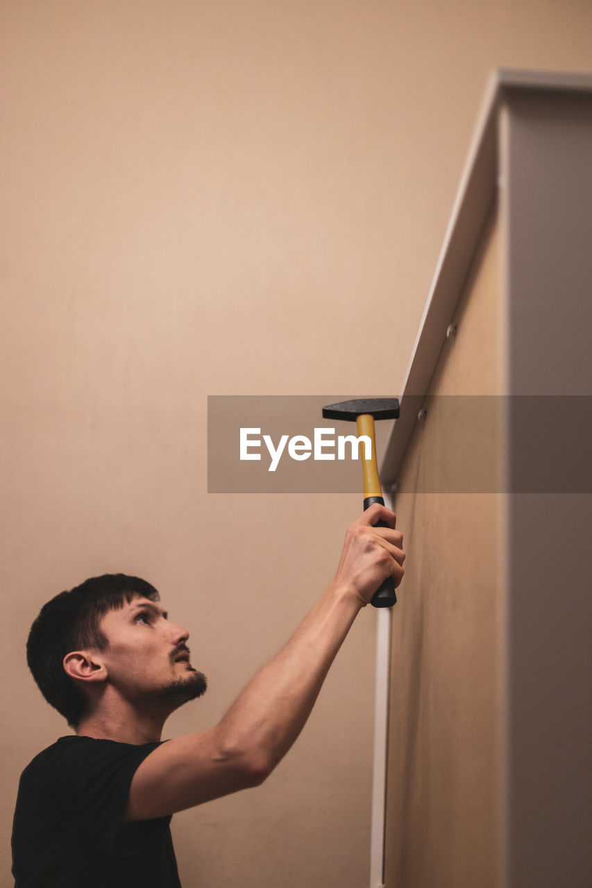A young man hammers rivets into a closet with a hammer.