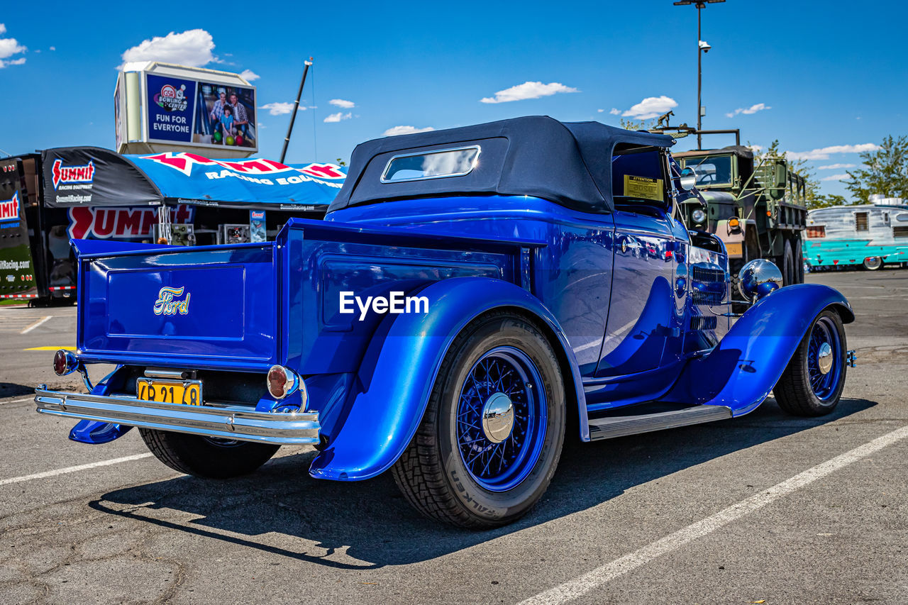 motor vehicle, car, vehicle, transportation, mode of transportation, land vehicle, antique car, blue, city, hot rod, street, road, vintage car, architecture, auto show, sky, touring car, sign, automobile, driving, day, truck, outdoors, travel