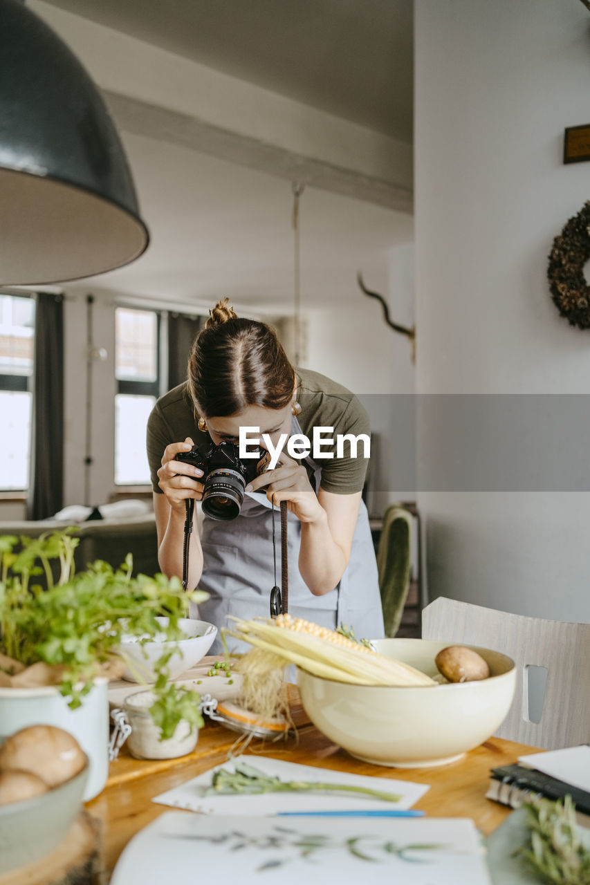 Young food stylist photographing through digital camera in studio