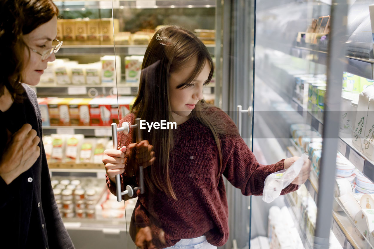 Daughter with mother buying food products while shopping in grocery store