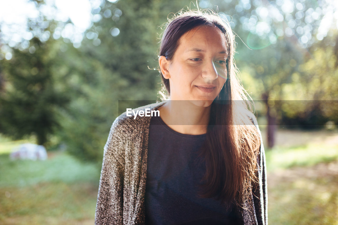 Portrait of smiling young woman standing against trees