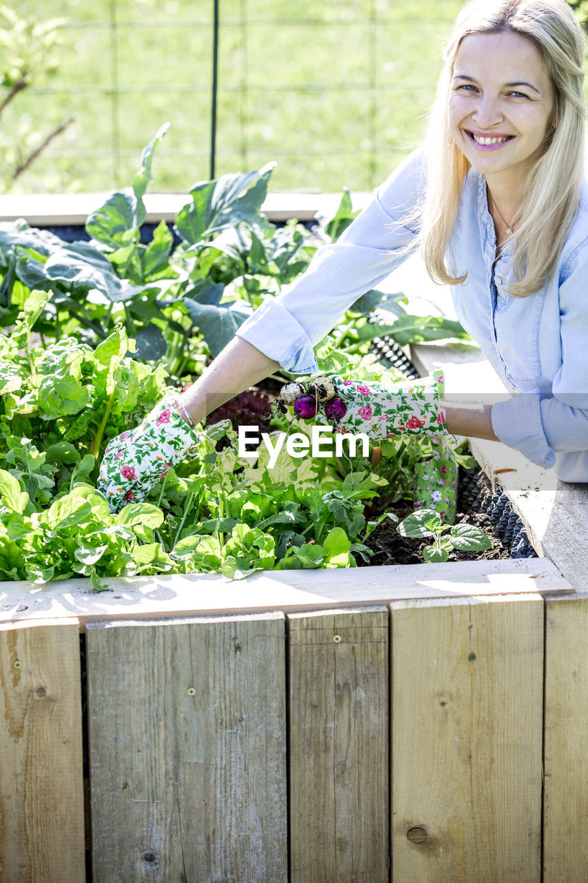 Woman gardening in wooden container at backyard during sunny day