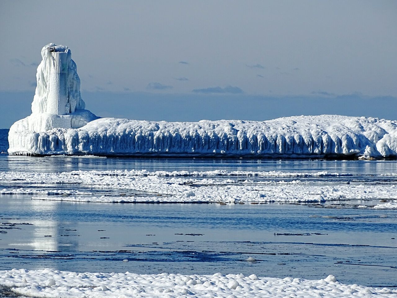 Frozen lighthouse and pier by lake michigan against sky