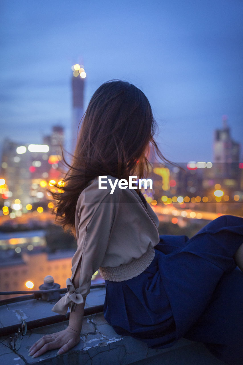 REAR VIEW OF WOMAN IN CITY AGAINST SKY AT NIGHT