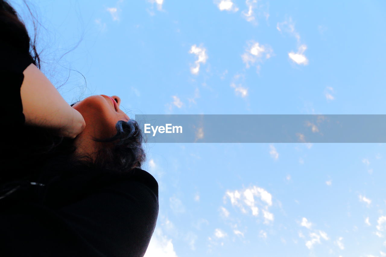 Low angle view of young woman with hand on chin against sky