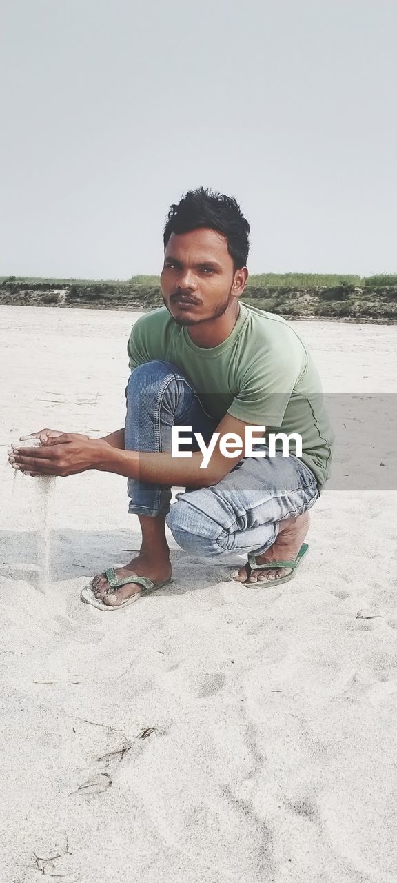 FULL LENGTH OF YOUNG MAN SITTING ON BEACH