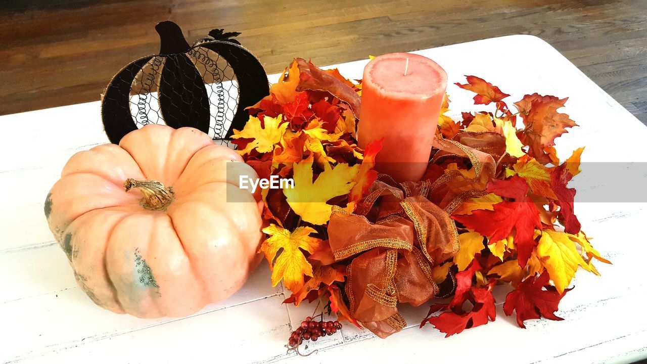 High angle view of pumpkin and candle amidst autumn leaves on table