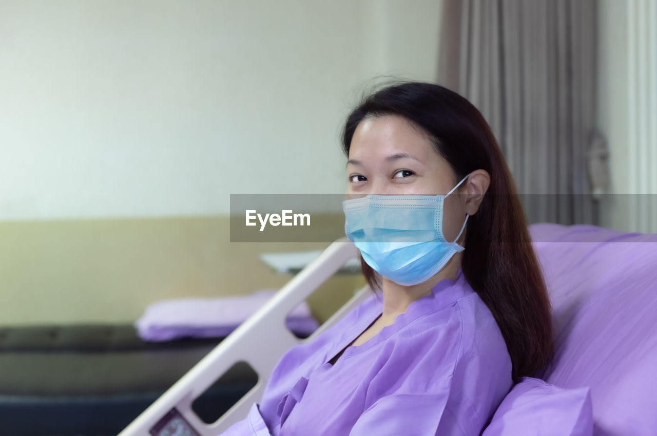 Female patient is smiling and showing medical mask in hospital room. medical healthcare concept.