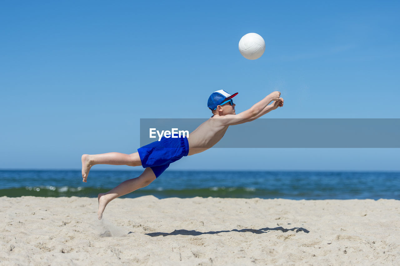 Full length of boy playing volleyball against sea