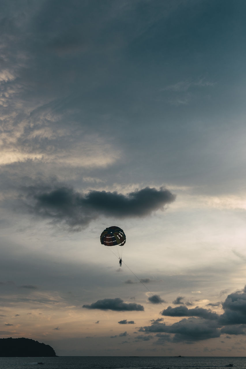 Low angle view of person in parachute over sea during sunset against cloudy sky