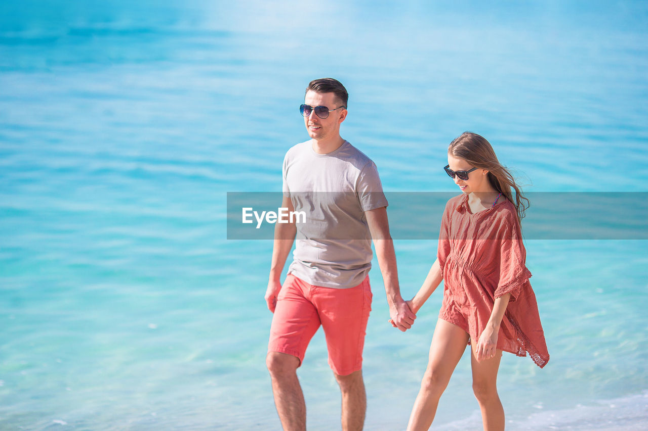 Father holding hand with daughter walking on beach