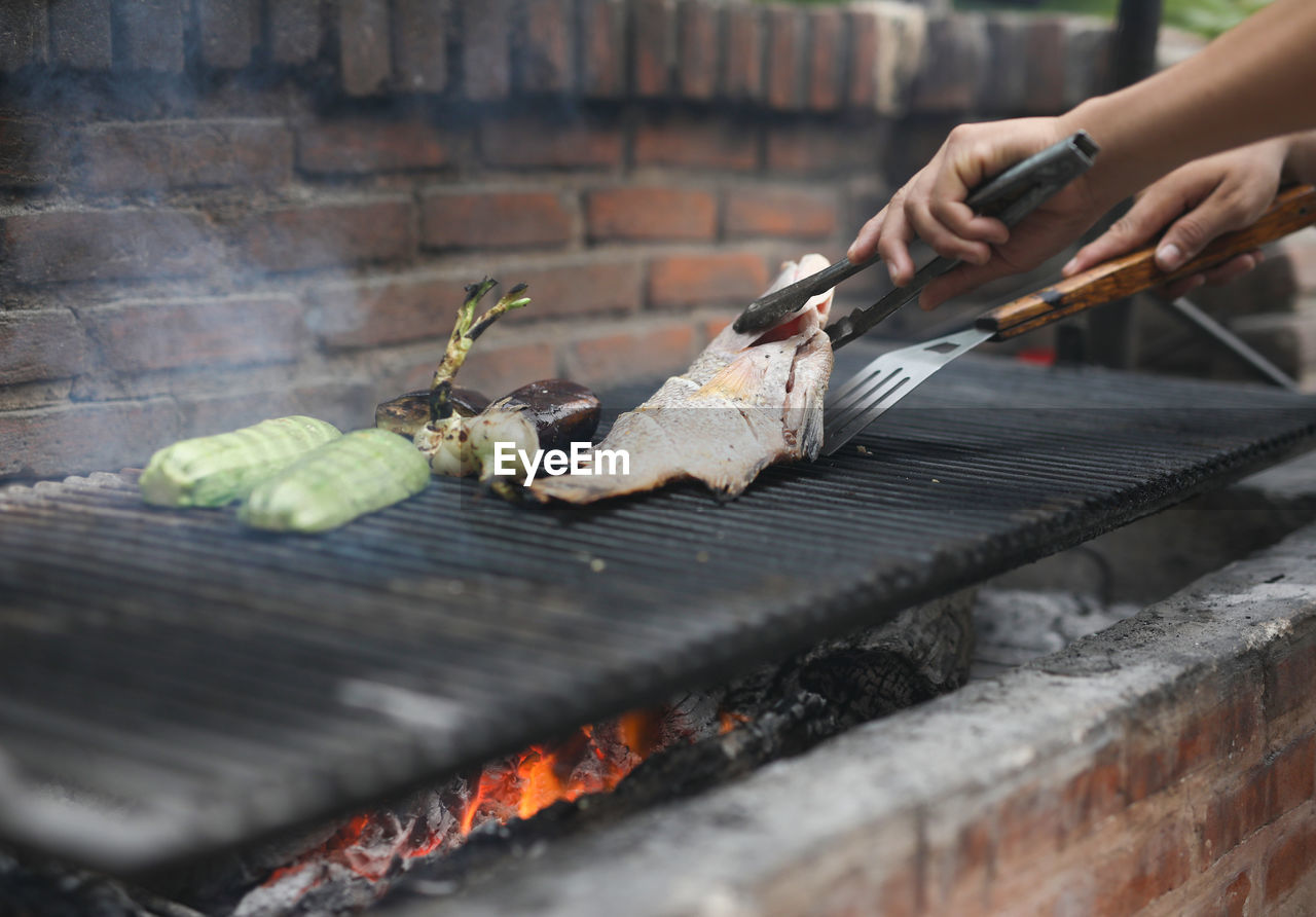 Close-up of man preparing fish on barbecue grill