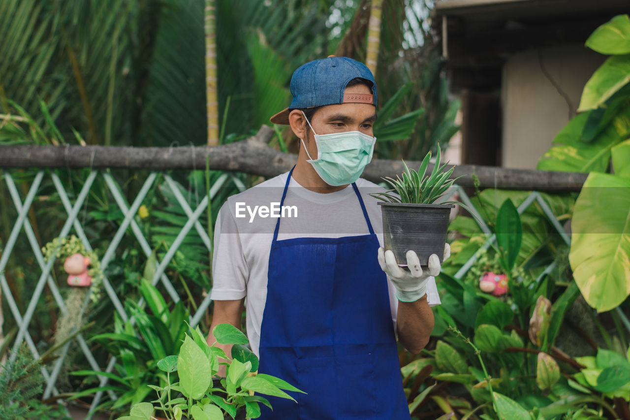 Botanist wearing mask holding potted plant at shop