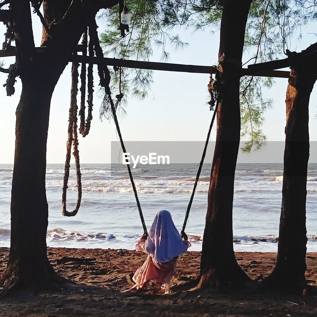 Rear view of woman on tree trunk by sea