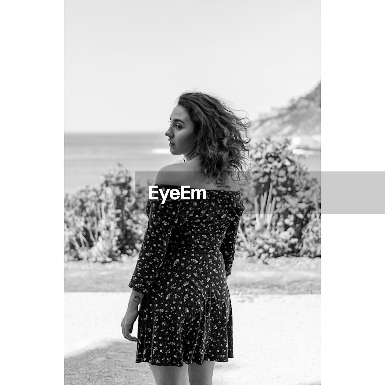 YOUNG WOMAN LOOKING AWAY WHILE STANDING ON ROCK