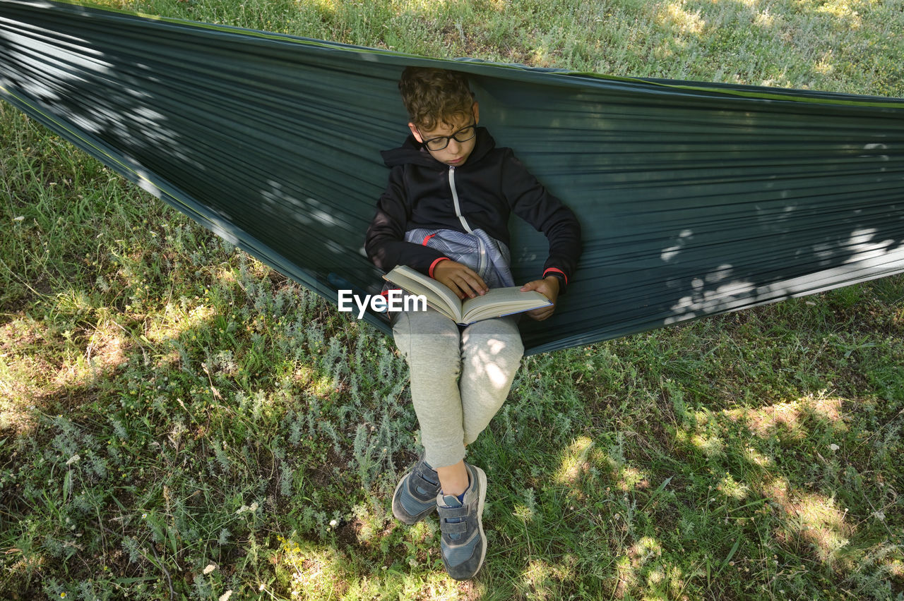 Little boy reading book and relaxing in hammock