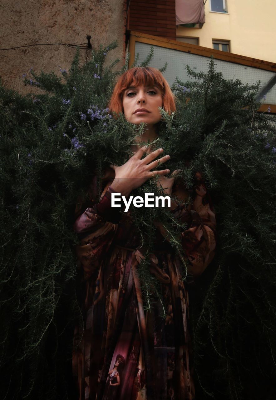 Portrait of young woman standing against plants