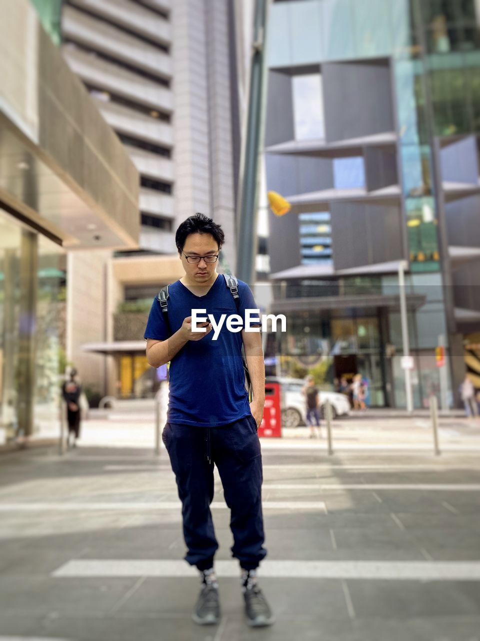 Portrait of young man walking on street in city and using smartphone.