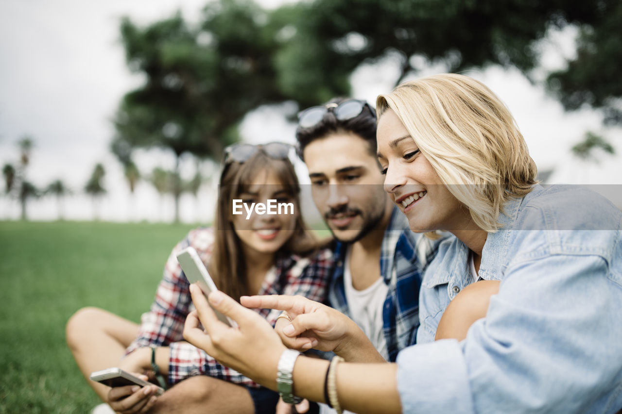 Young woman with friends using phone on field