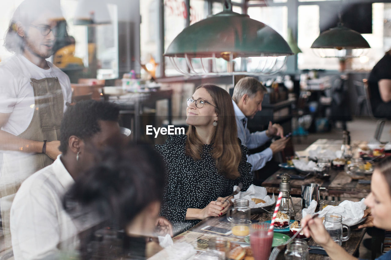 Waiter standing by customers at restaurant seen from window